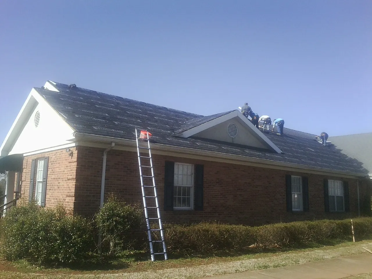 Crew tearing shingles off a brick ranch roof with a ladder set — Emergency Roof Repair work by our crew in Fincastle