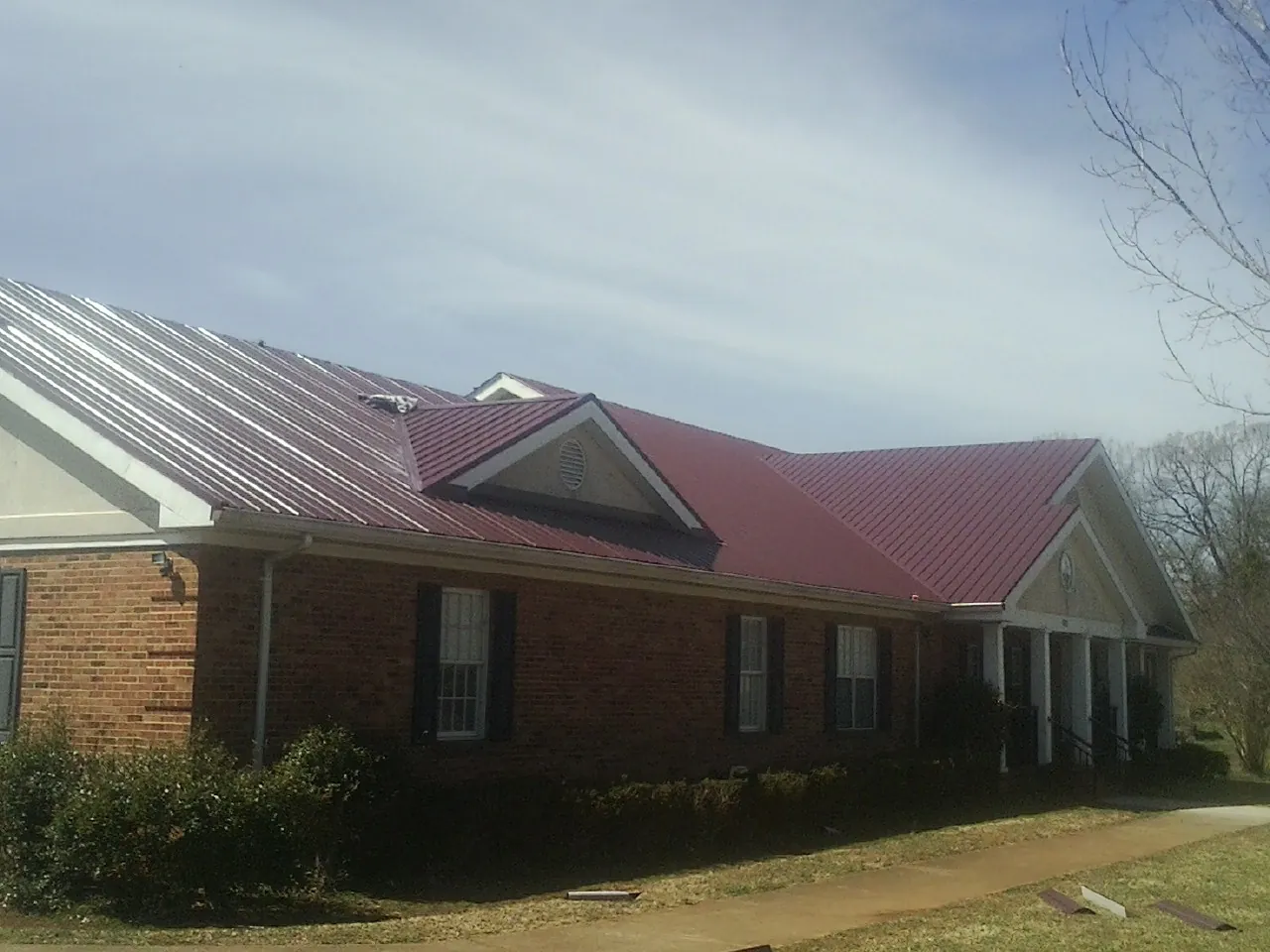 Red metal roof with gabled entries on a long brick building, from a Hail Damage Roof Repair job in Fincastle