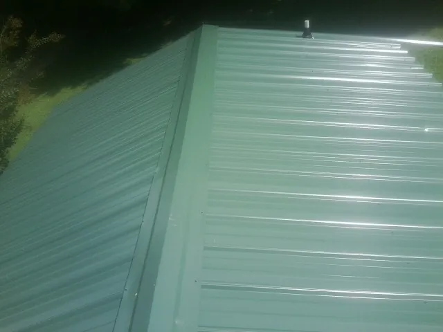 New green metal panels meeting at the ridge of a roof — Flat Roof Repair work by our crew in Fincastle