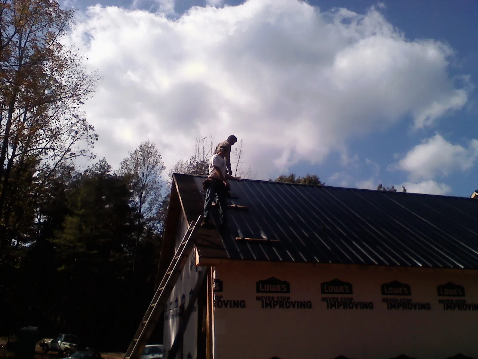 Roofer fastening dark metal panels high against a cloudy sky, from a Roof Inspection job in Fincastle