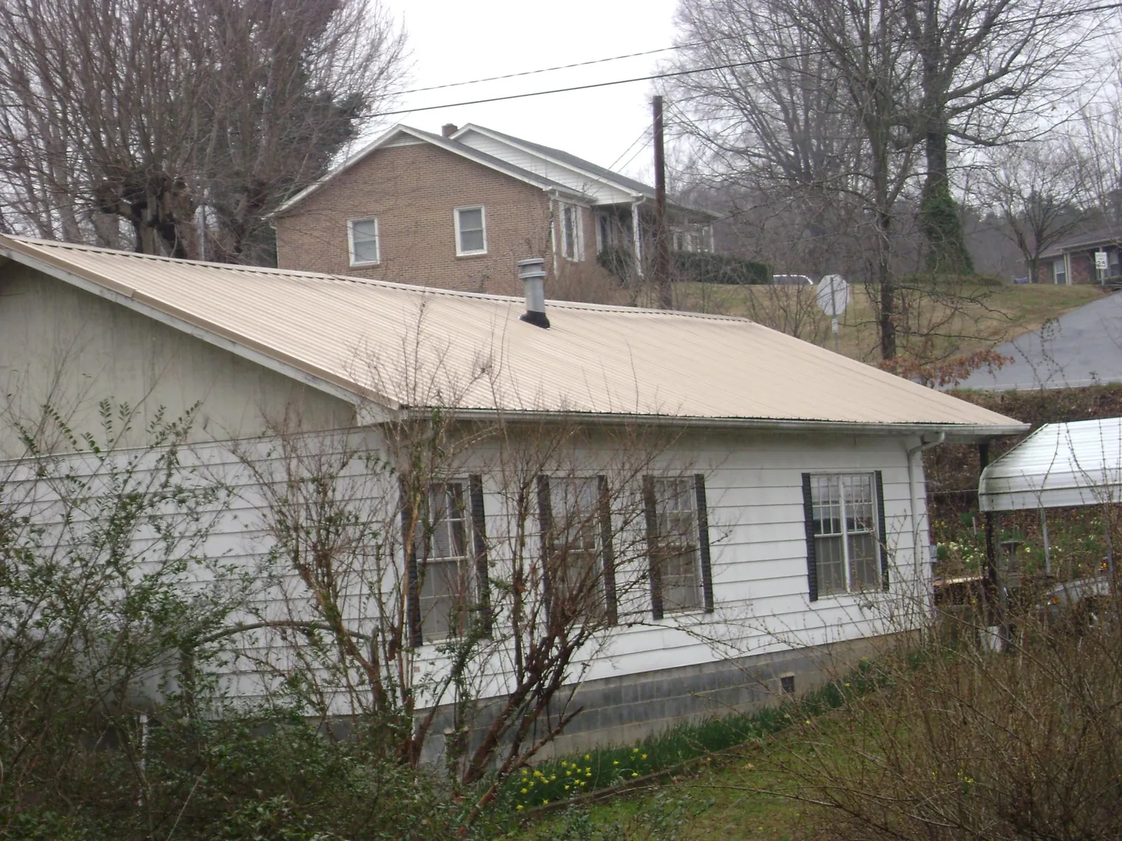 Tan metal roof on a white sided house set into a hillside — Commercial Roofing by Roofing Brothers in Fincastle